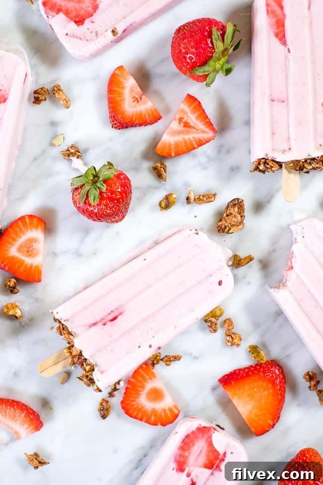 Creamy strawberry popsicles with granola on the bottom and fresh strawberries