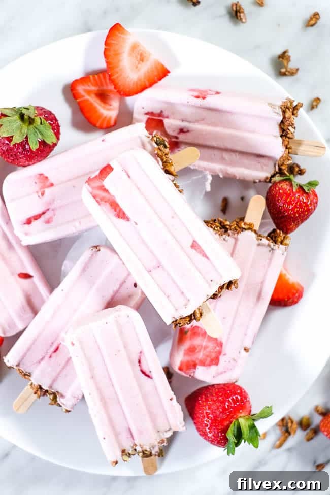 Creamy strawberry popsicles with granola on the bottom and fresh strawberries on a plate.