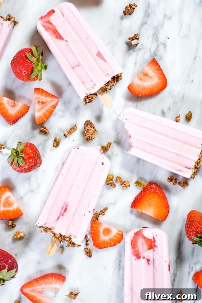 Creamy strawberry popsicles with granola on the bottom and fresh strawberries