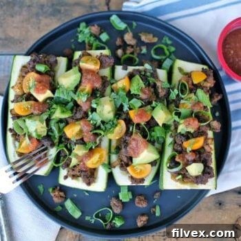 Close-up of baked taco zucchini boats filled with seasoned meat and fresh toppings.