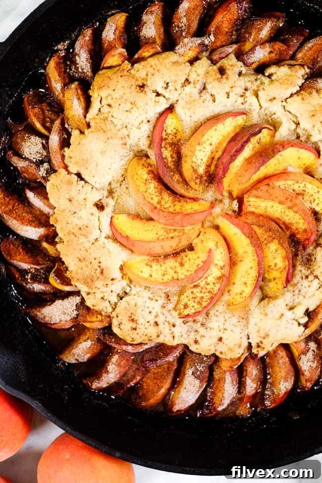 Gluten free peach cobbler in cast iron skillet with extra peaches on top and cinnamon. 