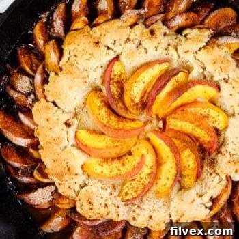 Gluten free peach cobbler in cast iron skillet with extra peaches on top and cinnamon. 