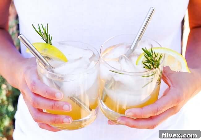 Holding two glasses of this lemon & rosemary cocktail with stainless steel straws in glasses. 