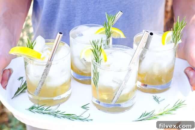 Holding a tray with four glasses of iced lemon & rosemary cocktail with lemon wedges, fresh rosemary and stainless steel straws. 