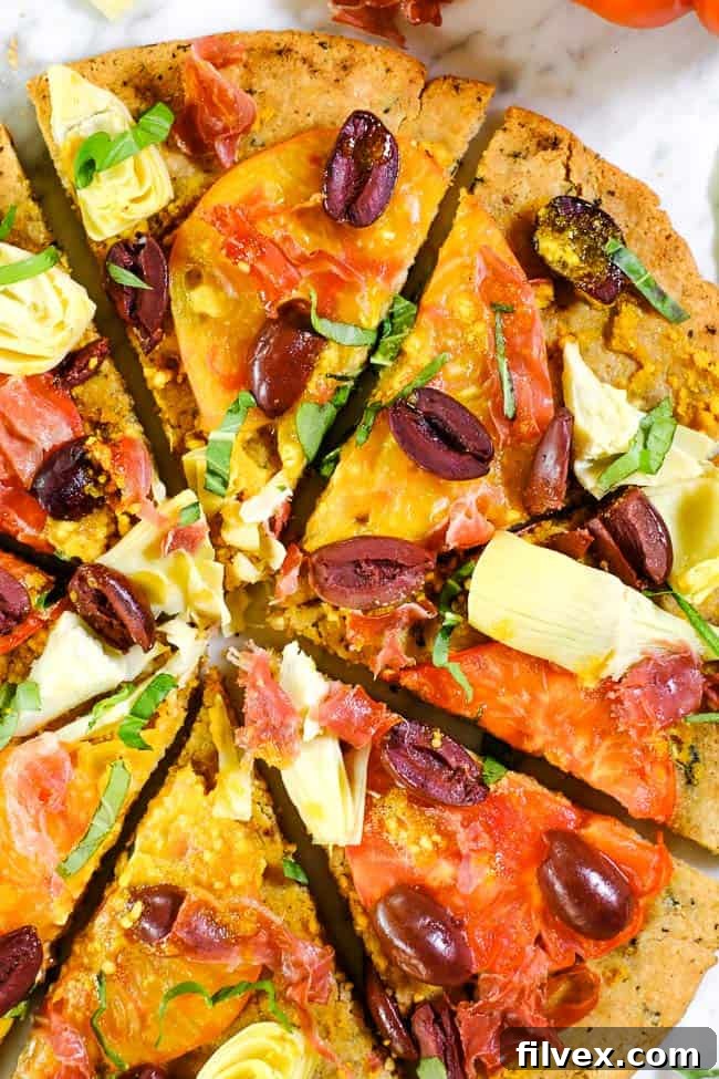 Close-up of a grilled paleo pizza loaded with vibrant heirloom tomatoes, tender artichoke hearts, briny kalamata olives, savory prosciutto, and aromatic fresh basil.