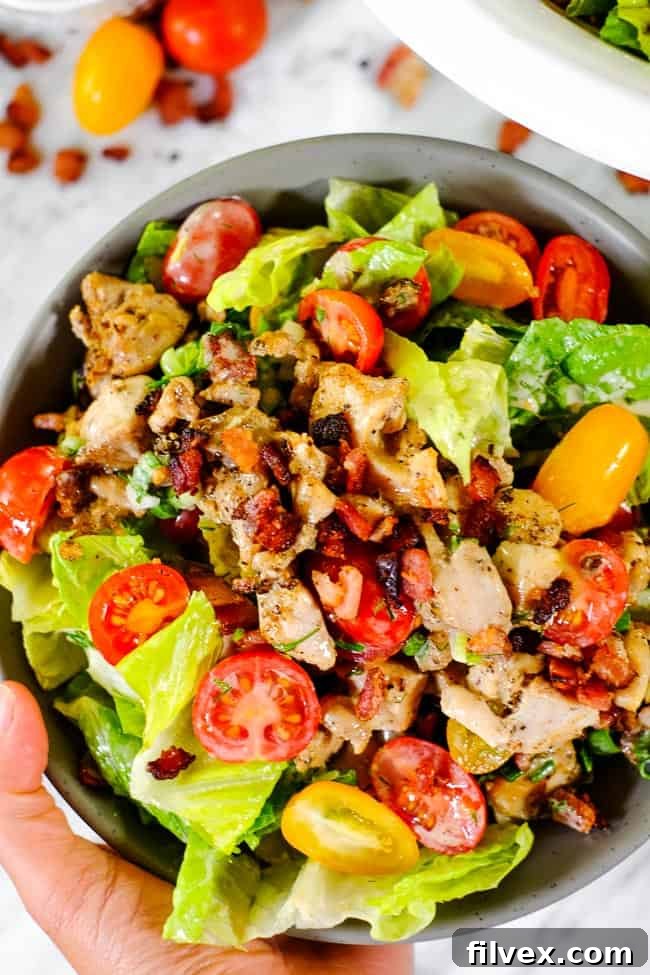 A person holding a bowl of freshly prepared BLT salad, with a focus on the vibrant ingredients and creamy texture of the dressing.