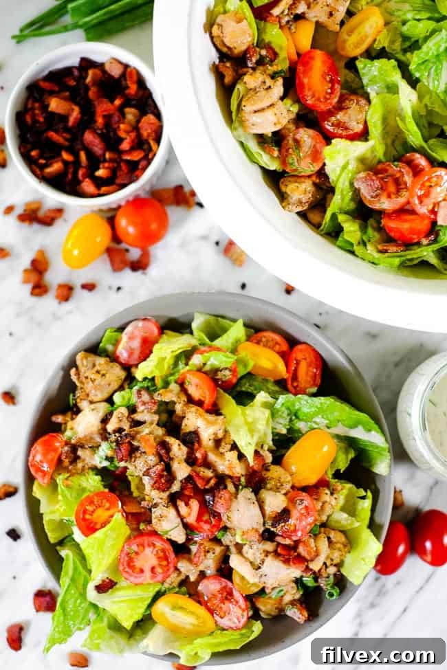 A BLT salad bowl placed next to a larger serving bowl, with extra crispy bacon, ripe tomatoes, and a small dish of creamy dressing on the side.