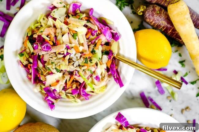 A vibrant bowl of Whole30 and Paleo compliant coleslaw, featuring shredded cabbage, carrots, and jicama, tossed in a zesty, mayo-free Italian dressing. Fresh lemons, shredded carrots, and purple and green cabbage are artfully arranged around the bowl, highlighting the natural ingredients of this healthy and easy-to-prepare salad.