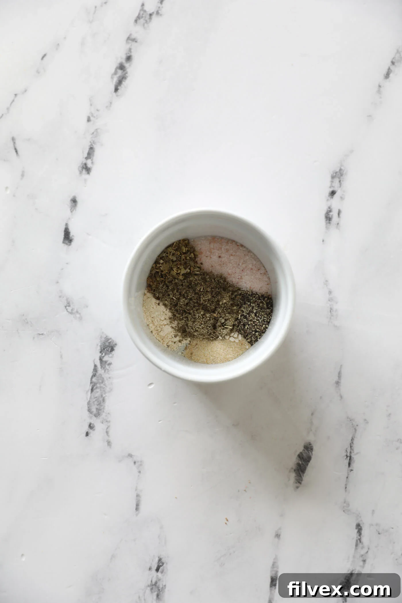 A small bowl containing the dry seasoning ingredients for breakfast sausage, ready to be mixed.