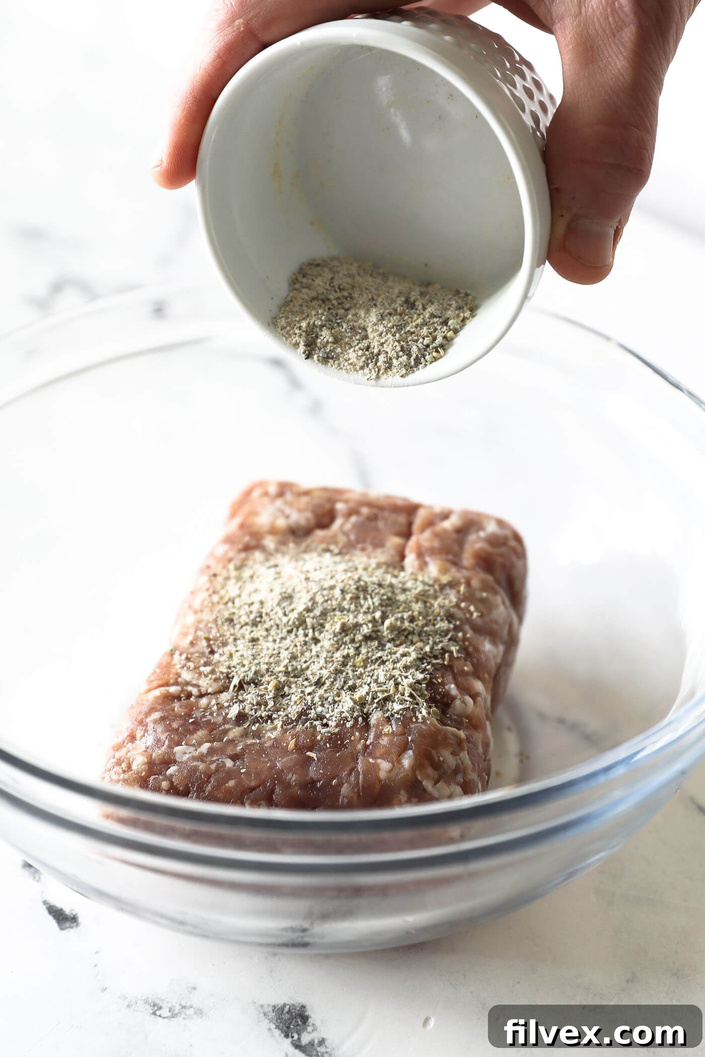 Ground pork placed in a mixing bowl with the prepared seasoning blend sprinkled over it.