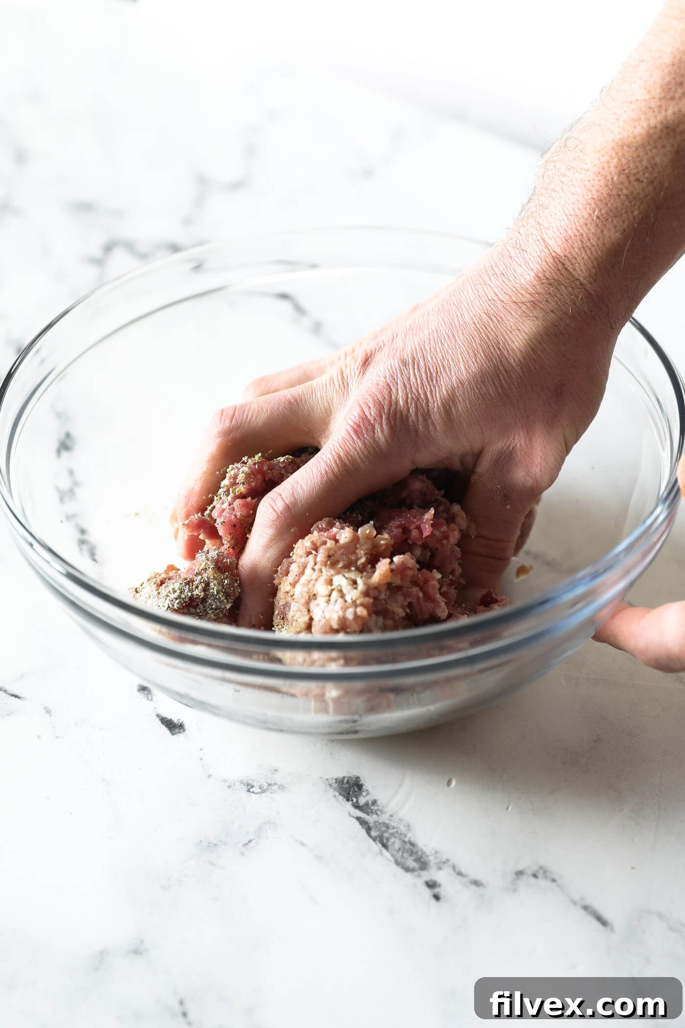 Hands gently mixing the seasoning into ground pork in a bowl to ensure even distribution.