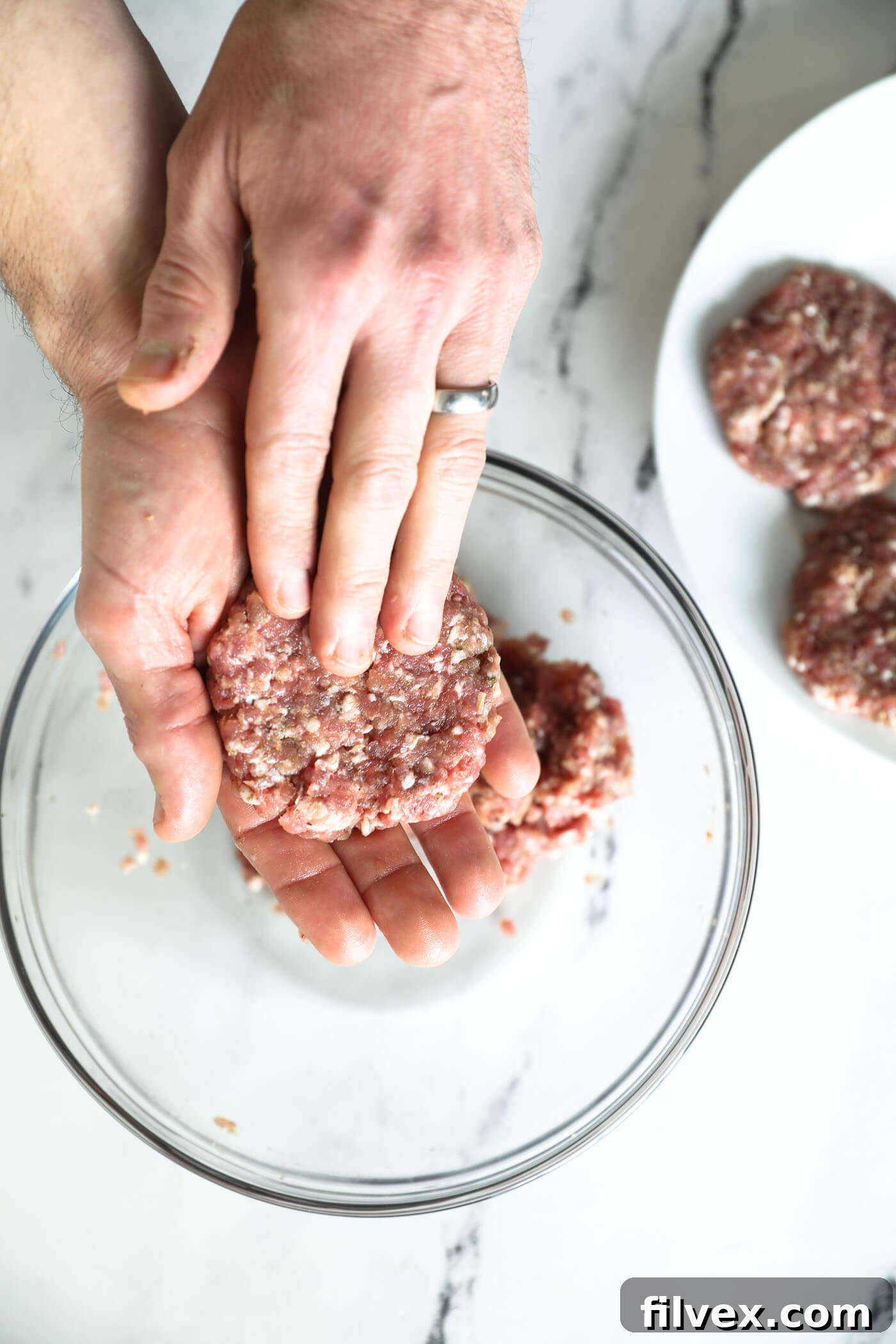 A hand shaping a portion of seasoned ground pork into a perfectly round breakfast sausage patty.