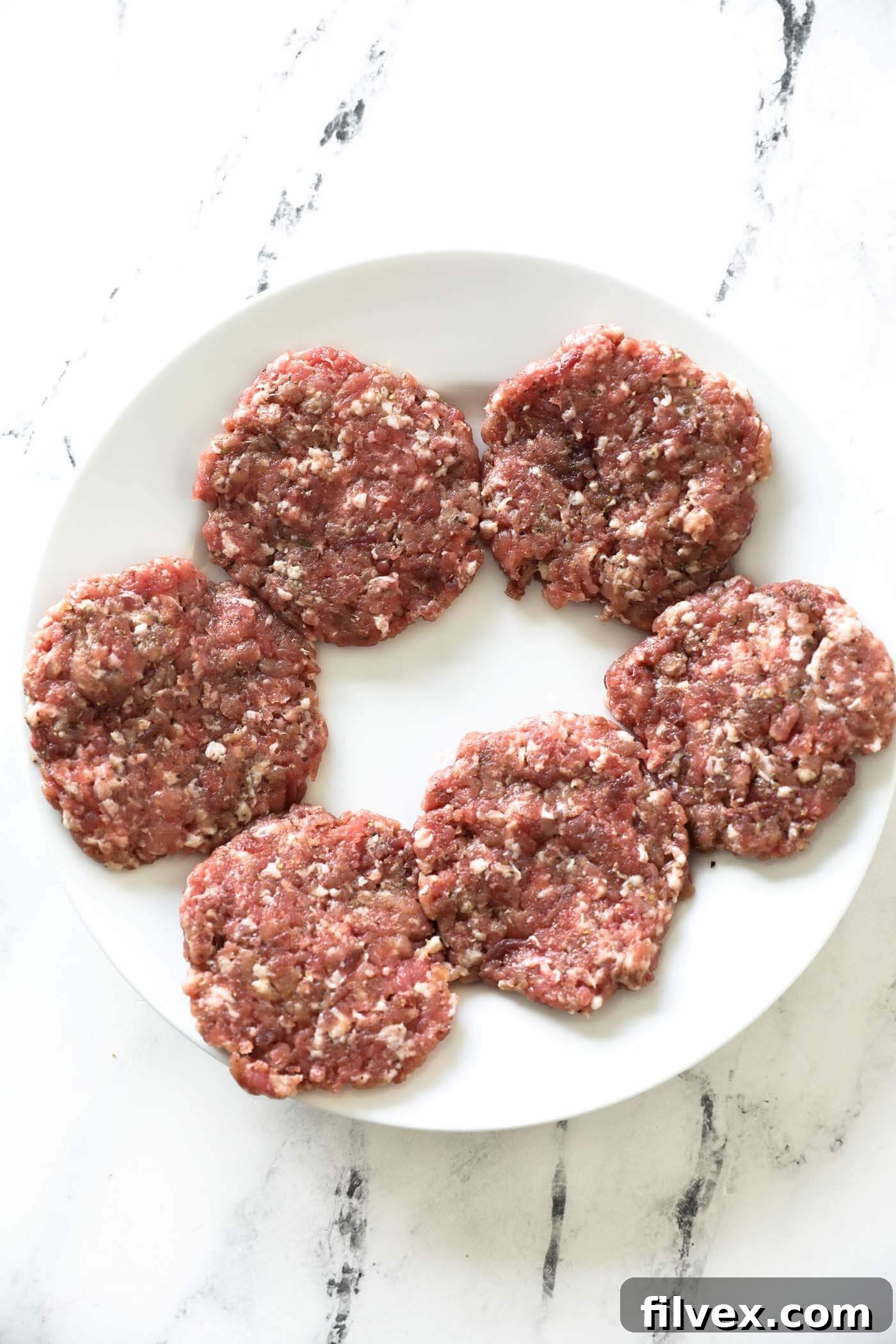 Six homemade breakfast sausage patties neatly arranged on a cutting board, ready for cooking.