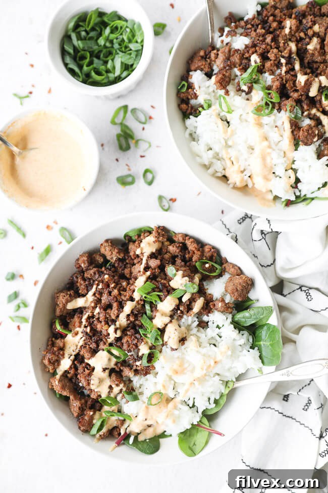 Two bowls of Korean beef with rice and greens, topped with chopped green onion and a spicy mayo sauce.