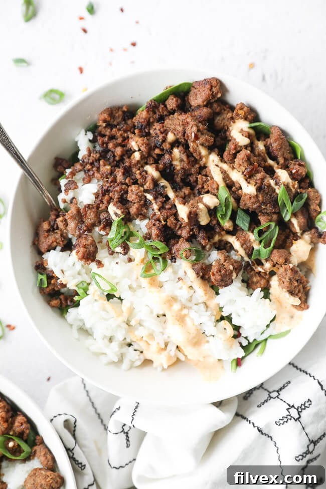 Close up of one bowl of Korean beef over rice and greens. Topped with chopped green onion and spicy mayo.
