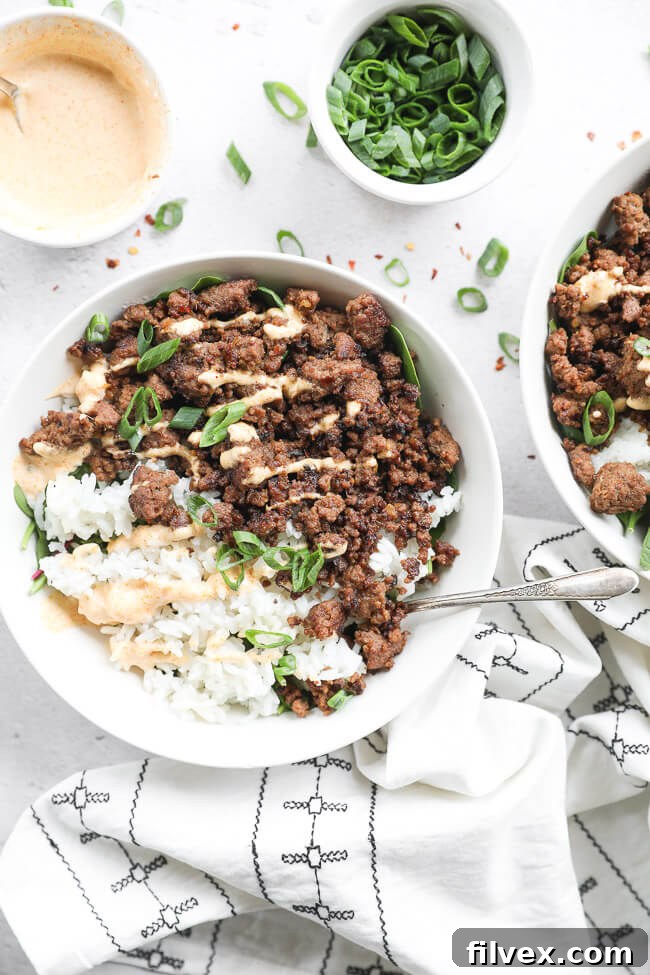 Korean beef served in a bowl with rice and greens. Topped with chopped green onion and drizzled with spicy mayo.
