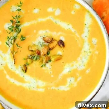 Close up shot of carrot ginger soup with tzatziki sauce, pistachios and fresh thyme.