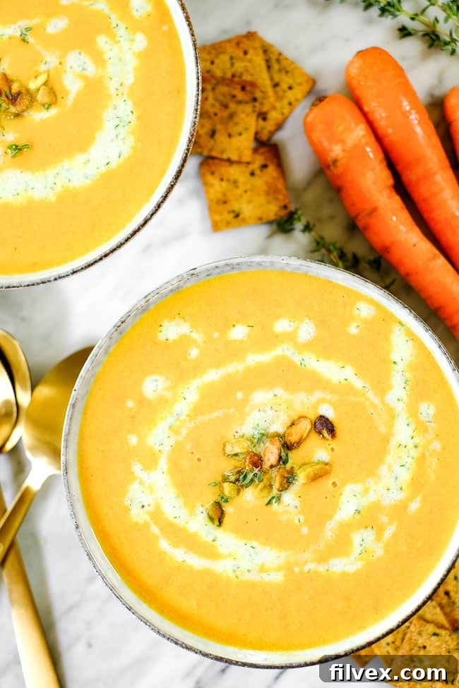 Two cozy bowls of carrot ginger soup, each garnished with dairy-free tzatziki, pistachios, and fresh thyme, artfully displayed on a wooden surface.