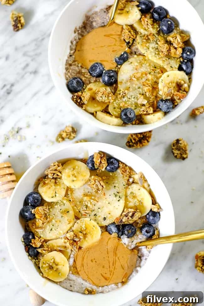 Two enticing bowls of Chai Spiced Paleo Chia Seed Pudding, each brimming with an assortment of fresh banana slices, delicate pear pieces, vibrant blueberries, crunchy grain-free granola, and a generous swirl of rich nut butter, arranged for a shared breakfast or snack.