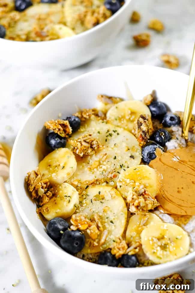 A vibrant, close-up shot of Chai Spiced Paleo Chia Seed Pudding artfully garnished with various toppings including sliced bananas, fresh blueberries, crisp pear slices, crunchy grain-free granola, and a luscious swirl of nut butter.