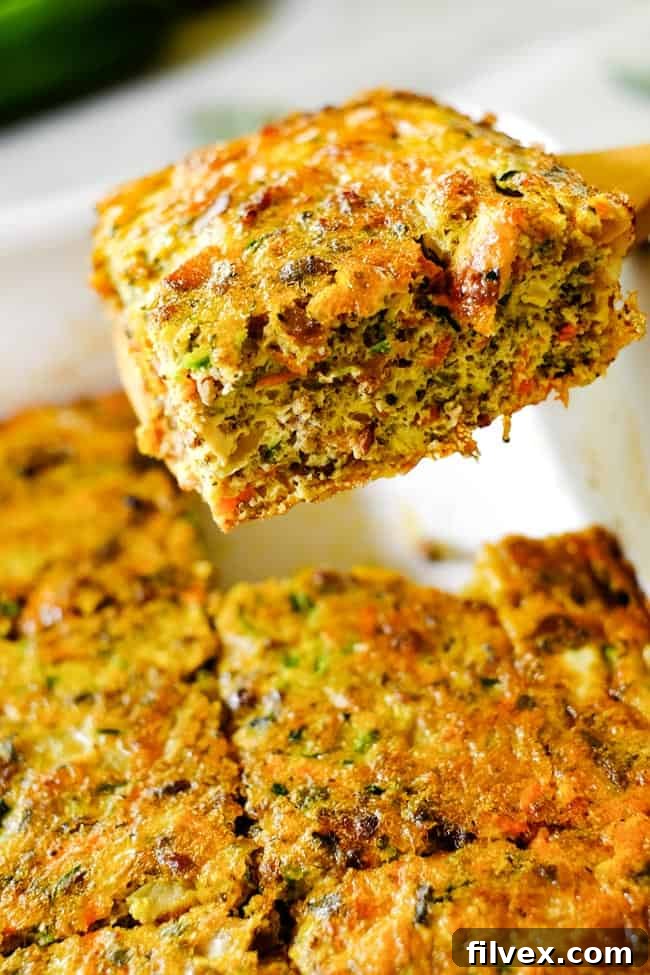 A piece of the Loaded Whole30 Breakfast Casserole being served from the pan with a spoon, showing its layered ingredients and golden edges.