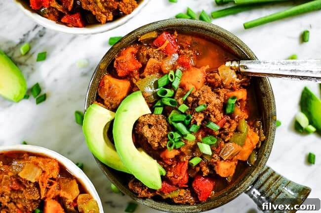 Paleo + Whole30 sweet potato chili served up in bowls with chopped green onion and avocado slices. A hearty, healthy meal perfect for fall and winter comfort.