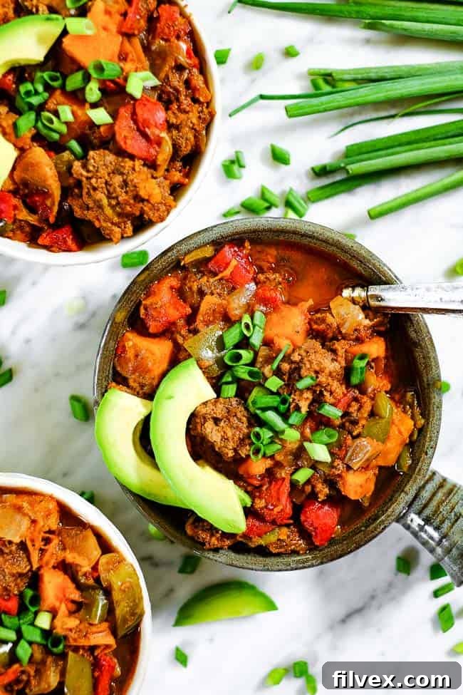 Paleo + Whole30 sweet potato chili in bowls with chopped green onion and avocado slices, perfectly portioned and ready to be served or enjoyed as leftovers.