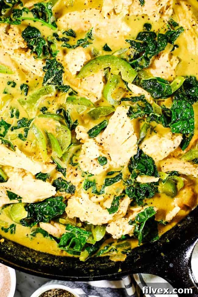 Close up shot of Thai coconut curry in cast iron skillet. Chicken, onion, bell pepper and kale in a creamy curry sauce.