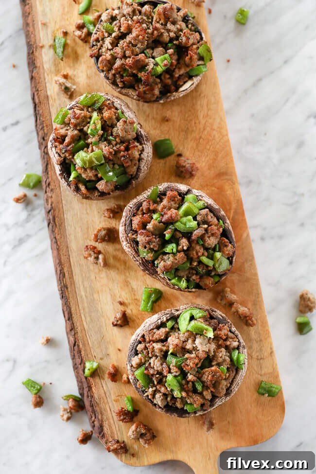 Overhead vertical shot of two baked sausage stuffed portobello mushrooms on a wooden board, garnished with fresh green peppers.