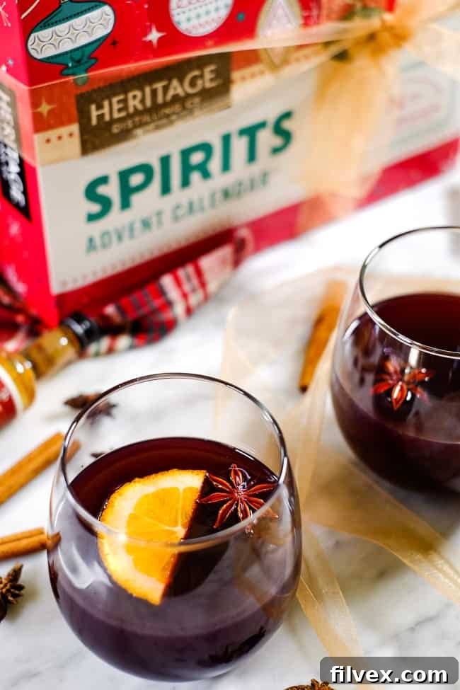 Simple mulled wine recipe in glasses garnished with orange slices and star anise. Cinnamon sticks and Heritage Distilling Company advent calendar in the background. 