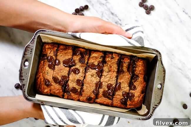 Golden-brown Paleo chocolate chip banana bread loaf cooling in a parchment-lined bread pan, ready to be sliced and enjoyed.