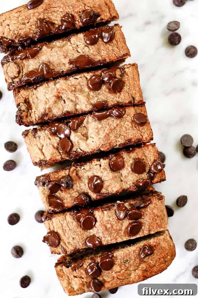 A freshly baked loaf of Paleo chocolate chip banana bread, perfectly sliced to reveal its moist texture and generous chocolate chips, resting on a wooden board.