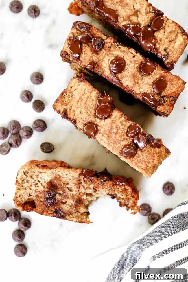 Several slices of Paleo chocolate chip banana bread, one with a bite taken out, showing the rich chocolate chips and soft texture, scattered on a wooden surface.