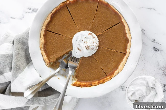 Delightful dairy-free and gluten-free pumpkin pie, perfectly baked in a pie dish, adorned with fluffy whipped coconut cream. One tempting slice is missing, with two forks poised, ready for another delicious bite. A true holiday centerpiece.