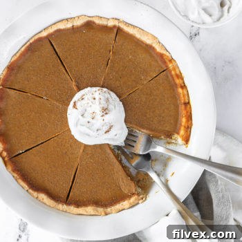 Dairy free and gluten free pumpkin pie in pie dish with whipped coconut cream on top. One slice of pie missing from dish and two forks dug into the missing spot.