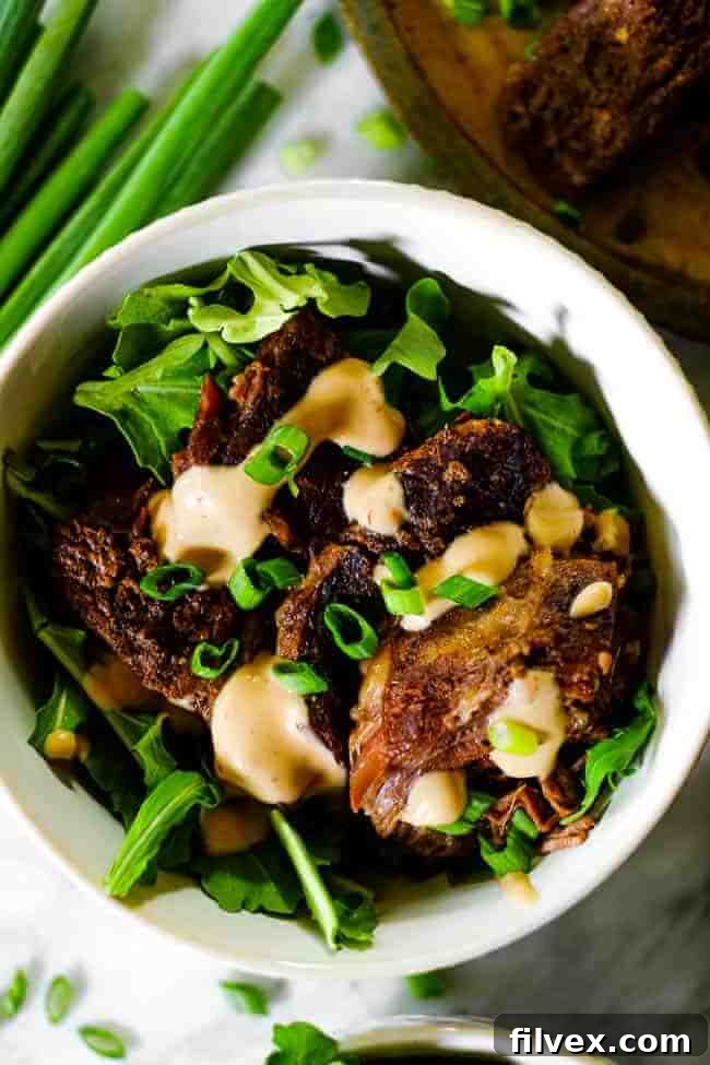 Close up overhead shot of instant pot short ribs in a bowl with greens, mayo sauce and chopped green onion.