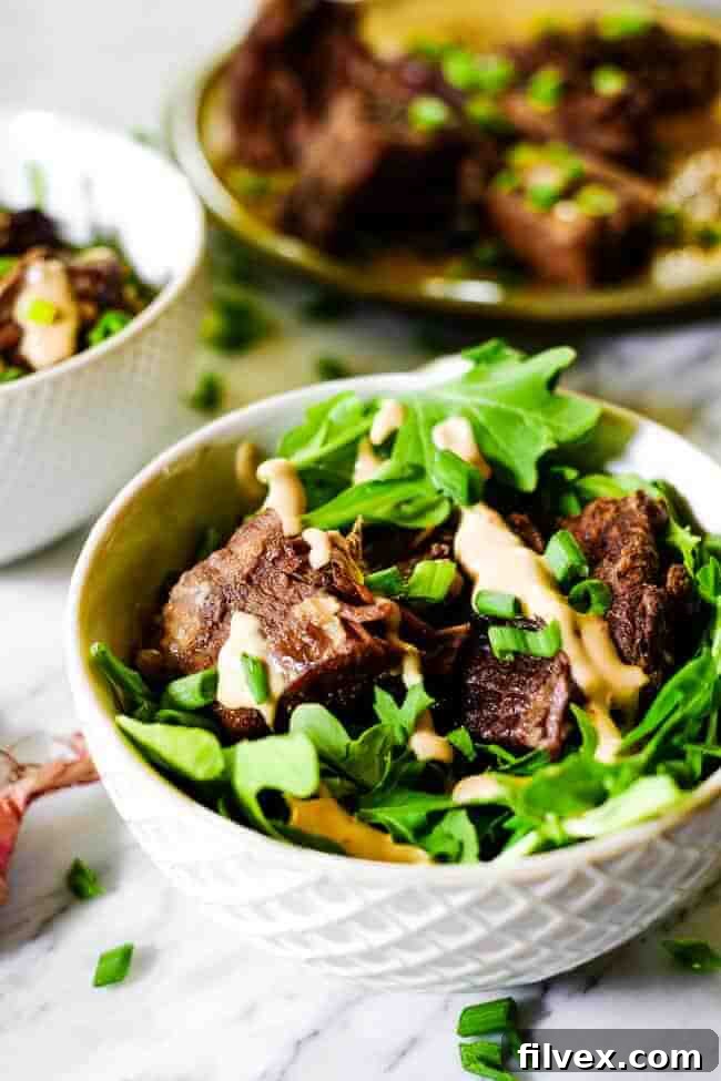 Instant pot short ribs served in a bowl with greens and topped with mayo sauce and chopped green onion.