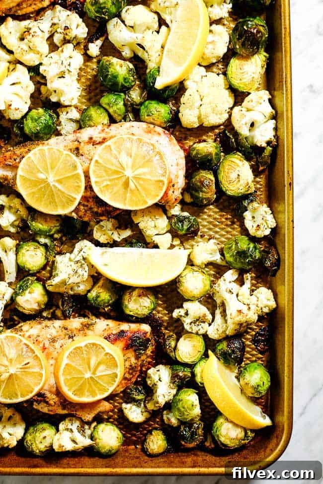 Easy lemon chicken and roasted brussels sprouts and cauliflower on a sheet pan with lemon slices. 