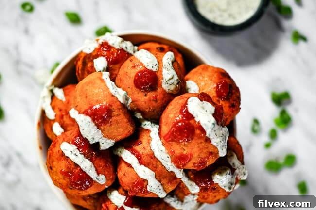 A bowl of baked keto buffalo chicken meatballs drizzled with creamy ranch and spicy hot sauce, garnished with fresh chopped green onion. A perfect low-carb appetizer or main dish.