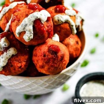 Plate of freshly baked buffalo chicken meatballs ready to be served, garnished with fresh green onions and a side of creamy ranch dipping sauce.