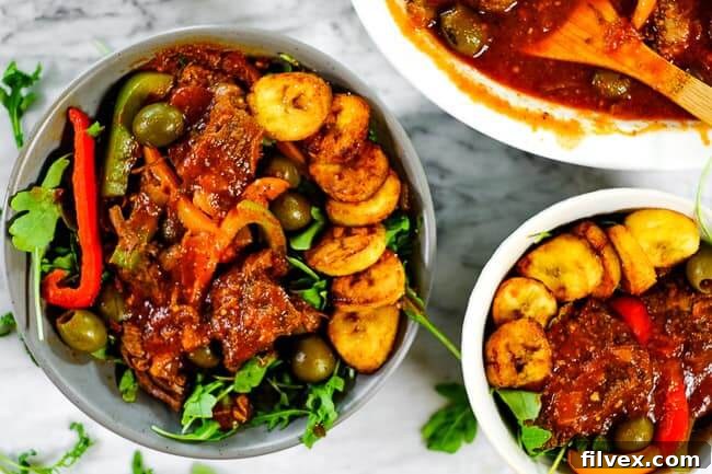 Ropa Vieja served in bowls with fresh greens and crispy fried plantains, highlighting the rich colors and textures of the dish.