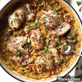 Vertical overhead image of skillet full of garlicky chicken in a creamy sauce with bacon.
