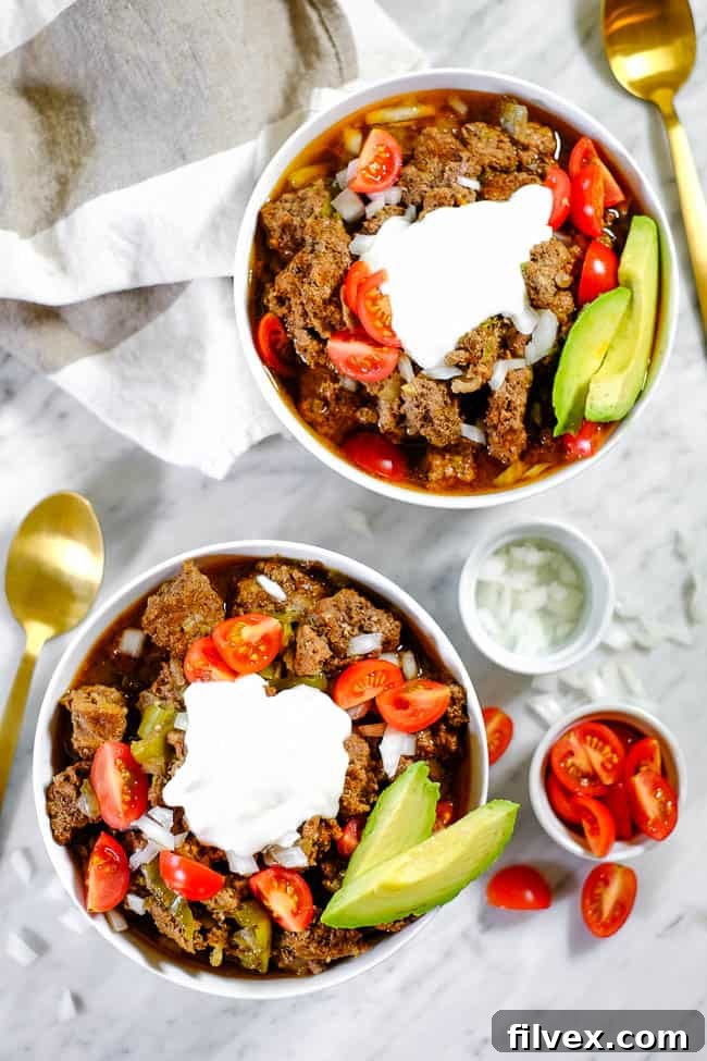 An overhead shot showcasing multiple bowls of delicious keto chili, beautifully presented with a variety of toppings including fresh chopped onion, juicy diced tomatoes, creamy avocado slices, and a dollop of dairy-free coconut yogurt. The arrangement highlights the versatility of this bean-free chili.