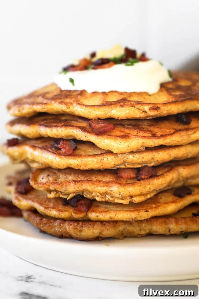 A perfectly stacked plate of crispy bacon pancakes, generously topped with sour cream, fresh chives, more crumbled bacon, and shredded cheese. This savory breakfast is ready to be devoured!