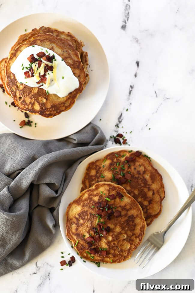 Two plates featuring delicious bacon pancakes. One plate is lavishly garnished with sour cream, crispy bacon bits, fresh chives, and melted cheese, while the other is simply topped with bacon and chives for a lighter touch.