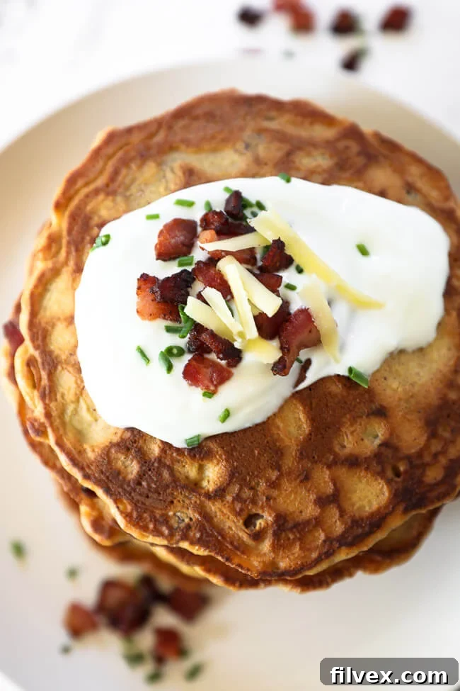 An inviting overhead shot of a single bacon pancake, beautifully adorned with a generous dollop of sour cream, crispy bacon crumbles, vibrant chives, and a sprinkle of cheese, highlighting the delicious texture and toppings.