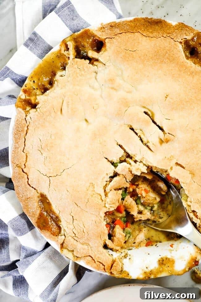 A golden-brown chicken pot pie casserole in a baking dish, with a scoop removed revealing the creamy filling and a serving spoon still in the dish.