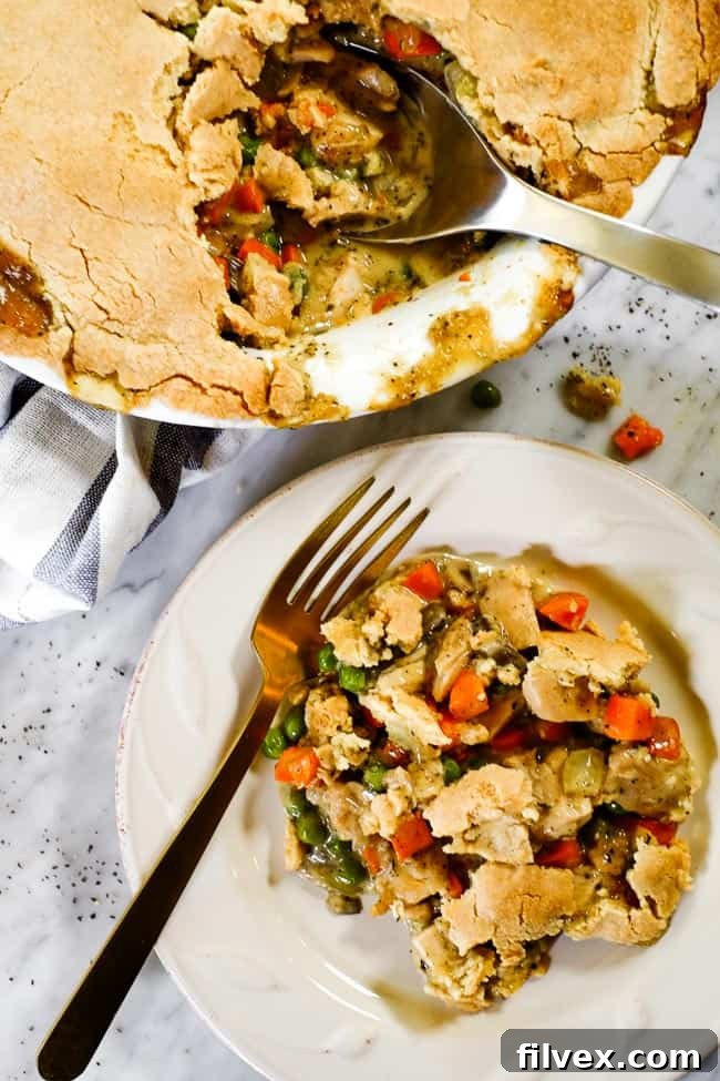 A serving of dairy-free chicken pot pie casserole on a plate with a fork, with the full casserole dish in the background with a blue striped towel.