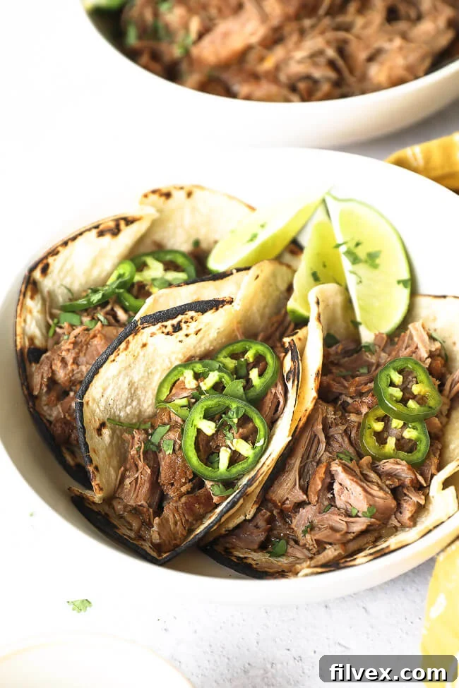 Angled image of three shredded pork tacos with sliced jalapeños and chopped cilantro on top. 