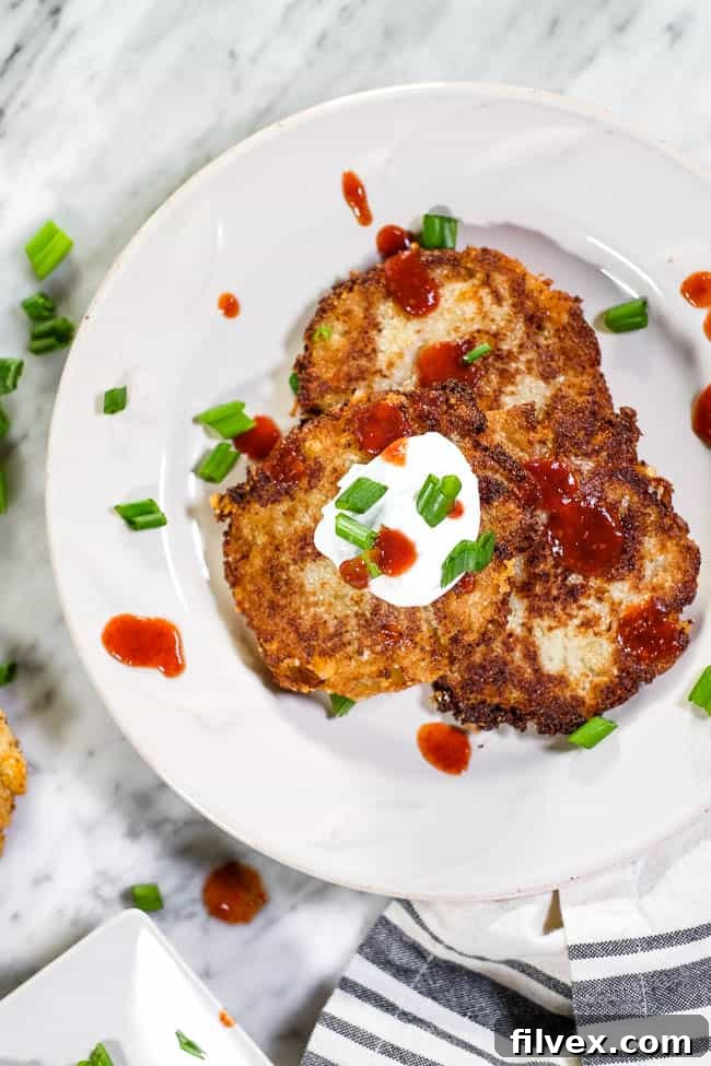 Cauliflower fritters on a plate topped with hot sauce, coconut yogurt and chopped green onion.